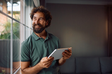 Happy man surfing the net on touchpad by window at home.