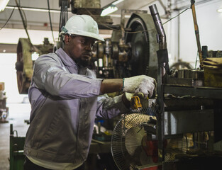 industrial worker wearing safety helmet uniform operate heavy machinery factory. worker equipped protective gloves has red walkie-talkie. background features complex mechanical equipment industrial.