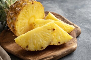 A halved pineapple sits beside three cut wedges on a rustic wooden board, resting on a mottled gray surface.  The fruit is ripe and golden yellow