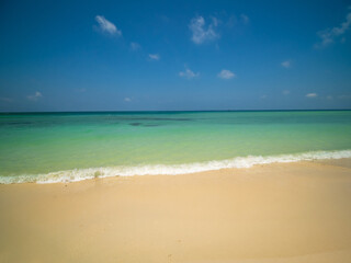 Peaceful tropical sea beach with gentle waves rolling onto golden sand under bright blue sky with fluffy white clouds. relaxing summer scene perfect scene for travel holliday and nature lovers
