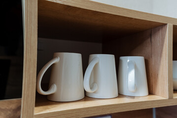 A set of modern minimalist white mugs is neatly displayed on a wooden shelf, enhancing your kitchens beauty and style while combining visual appeal with practicality for any home decor