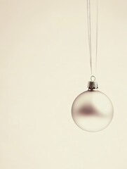 simple, beige elegant background with single shiny Christmas bauble hanging from a thin ribbon. Copy space