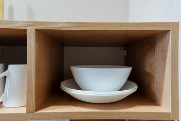 Discover a minimalist kitchen featuring stylish storage solutions, with elegant white dinnerware in a wooden cubby, balancing functionality and aesthetics to enhance the space beautifully
