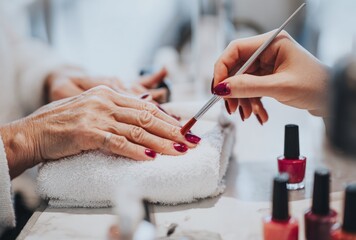 Close up of hands getting nails painted in a deep red color at a salon with light marble tables and white towels