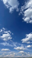 Obraz premium A sunny, vertical landscape view featuring a vast, bright blue sky dotted with fluffy, white cumulus clouds over a horizon line of green and yellow fields