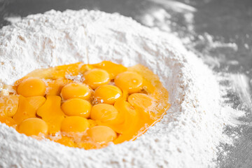 Raw eggs in a flour well on a stainless steel surface, ready for mixing. Classic setup for homemade...
