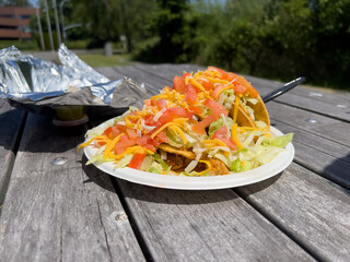 Close up angle of hot fresh Mexican street tacos served on a paper plate with foil on top of a wood picnic table.