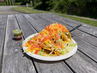 Close up angle of hot fresh Mexican street tacos served on a paper plate with foil on top of a wood picnic table.