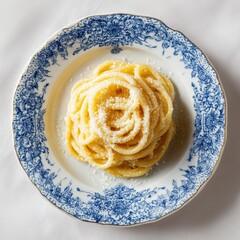 A plate of spaghetti aglio e olio, generously sprinkled with grated cheese, sits on a vintage blue and white patterned plate.  The pasta is golden and coiled in the center