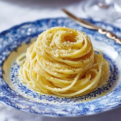 A plate of spaghetti aglio e olio, neatly coiled, topped with grated cheese and cracked black pepper, sits on a blue and white patterned plate