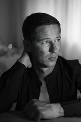 Fashion portrait of young man in black shirt poses over wall with contrast shadows