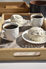 two cup of black coffee and two marshmallows on decorative white plates on marble surface tray