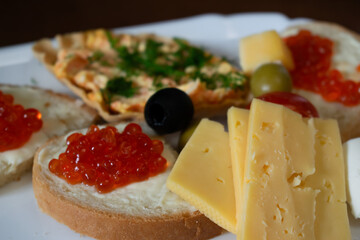 Sandwiches with red caviar, cheese and olives on a plate close-up