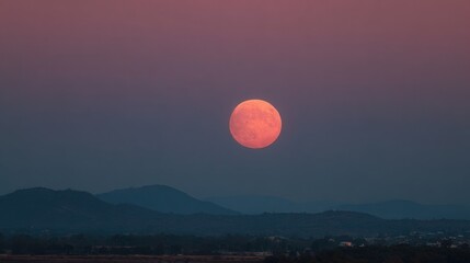 A full moon rises majestically above distant mountains during twilight, casting a warm glow over the tranquil landscape and enhancing the beauty of the evening sky.