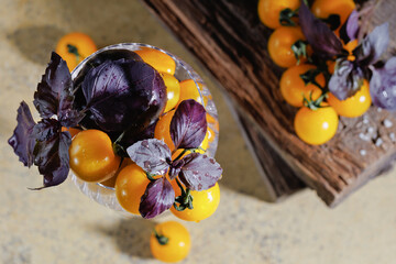 Above view of fresh yellow cherry tomatoes and wet basil leaves in a glass with wood textures