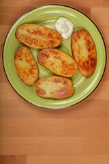 A high-angle shot shows a plate of golden brown baked potato halves and a dollop of sour cream on a...