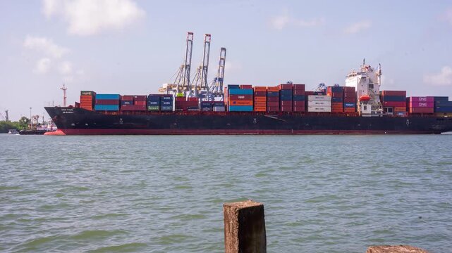 4K timelapse footage of cargo vessels and shipping container operations at Fort Kochi, Kerala, India. The scene captures bustling maritime trade with ships navigating the harbor, containers