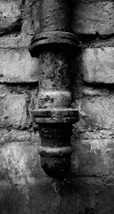 A weathered pipe affixed to a brick wall
