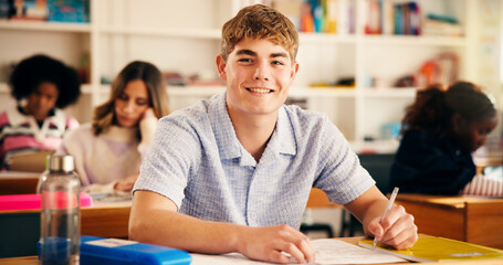 Happy, writing and portrait of boy teenager in classroom for learning, education or development....