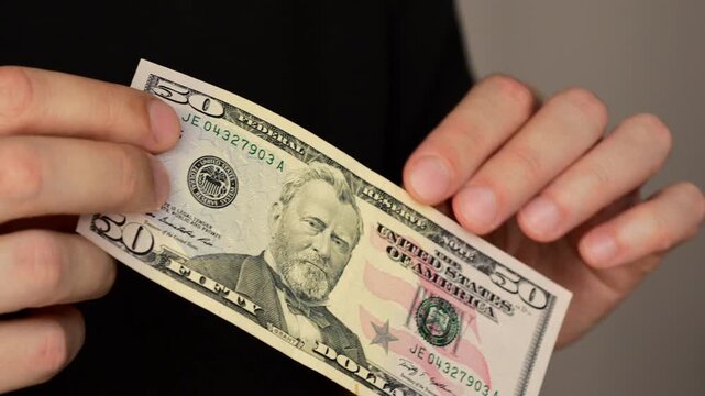 50 US dollars in the hands of a businessman.
Cash close-up.
Payment for goods and services in cash.
Expensive purchases and spending money.
Shopping and finances