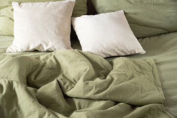 Two light pillows on green linen bedding with crumpled duvet.