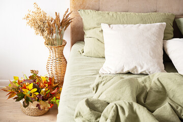 Cozy bedroom interior with green linen bedding and autumn decoration.