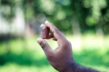 Hand holding a small piece of reddishbrown material outdoors