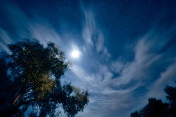 Obraz premium Clouds swirl around the moon, illuminated by its light, in the night sky.