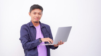 Happy asian man wearing purple t-shirt and holding laptop computer working online and looking at camera isolated on white background, online education