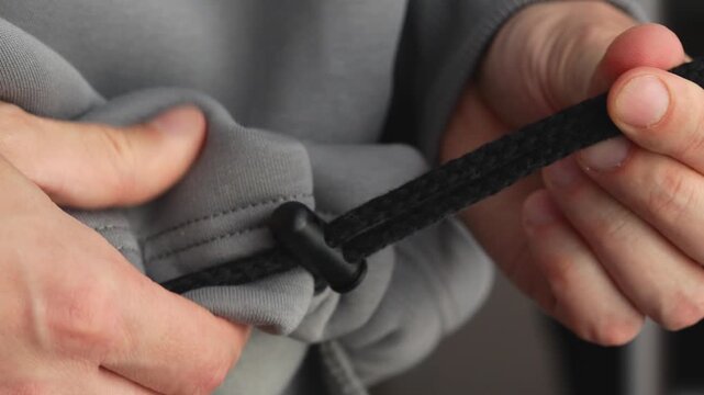 eyelet with a drawstring on a gray sports jacket.
A person tightens the drawstring on a jacket.
An elastic band on sportswear to adjust the size.
Clothes, eyelet, tighten, drawstring