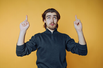portrait of young man dressed in a dark turtleneck is pointing upwards with a contemplative look on...