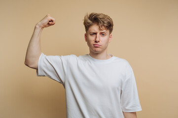 portrait of young man flexes his arm, showing off strength and confidence while wearing a casual...