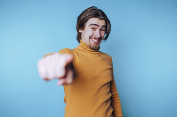 portrait of young man in an orange turtleneck smiles while pointing playfully at the camera,...