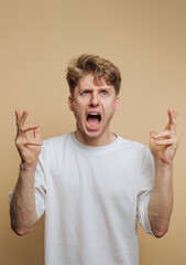 portrait of young man expressing hope and anticipation with crossed fingers, featuring an exuberant...