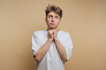 portrait of young thoughtful man is looking up with hands clasped, conveying a sense of hope and...
