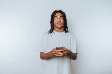 portrait of young man is appearing thoughtful while looking up at his phone screen, indicating...