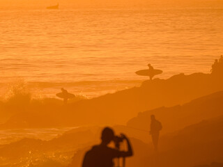 SILHOUETTE: Beach glows in intense golden light of a fiery sunset as surfers head back in the...