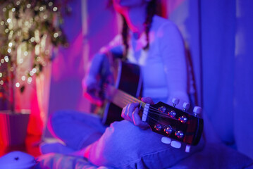 Female musician playing acoustic guitar at home, surrounded by vibrant neon lights, creating a lively and artistic atmosphere filled with passion and creativity