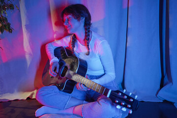 Female musician playing acoustic guitar, immersed in the joy of music while surrounded by vibrant...