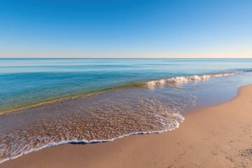 Obraz premium Tranquil beach scene at sunrise. Gentle waves lap at a pristine sandy shore. A vast, clear, turquoise-blue ocean stretches to the horizon beneath a vibrant, cloudless blue sky