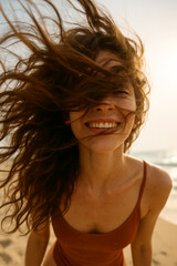 Joyful young woman smiling with her hair blowing wildly in the wind on a sunny beach, capturing a carefree and spontaneous summer moment