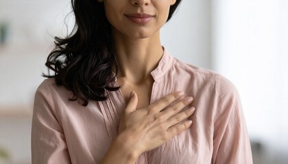 A Hispanic woman with a youthful and attractive appearance is captured in a close-up, cropped indoor shot, her folded palms on her chest expressing genuine feelings of gratitude