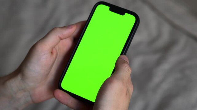 Smartphone with green screen in the hands of a man on a beige background.
Empty green screen for background replacement and for inserting ads.
Green chromakey on a smartphone
