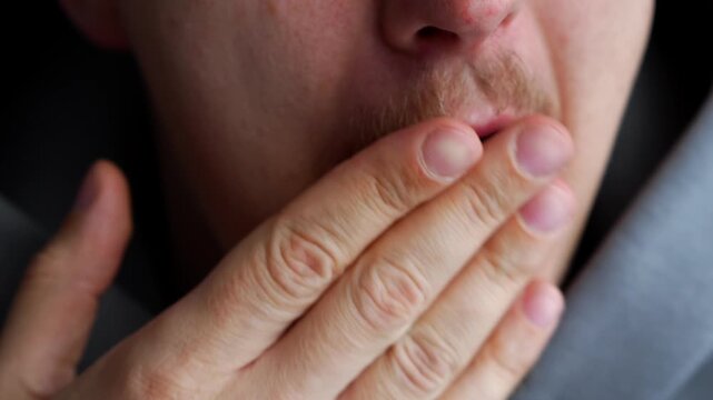 Man in gray coffee yawns in the room in the morning.
Sleepy man just woke up and yawns covering his mouth with his hand.
Close-up of a yawning man