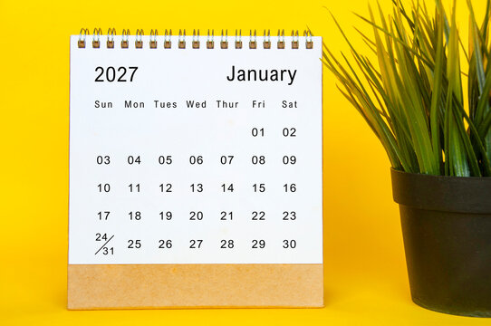 January 2027 calendar sheet with simple desktop setup, vibrant yellow edges, and potted plant beside.