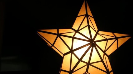 dramatic shot of single parol, geometric filipino christmas star lantern glowing brightly in dark room. festive decoration. symbol of celebration and light. greeting card, banner, holiday.