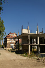 A bare, abandoned concrete building skeleton reaches for a blue sky, starkly contrasted by modern, completed residential buildings in the background. Illustrates urban development & decay.
