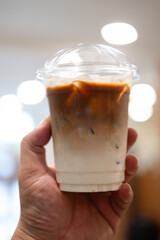 Someone holding a cup of iced cafe latte with two layer, espresso and fresh milk