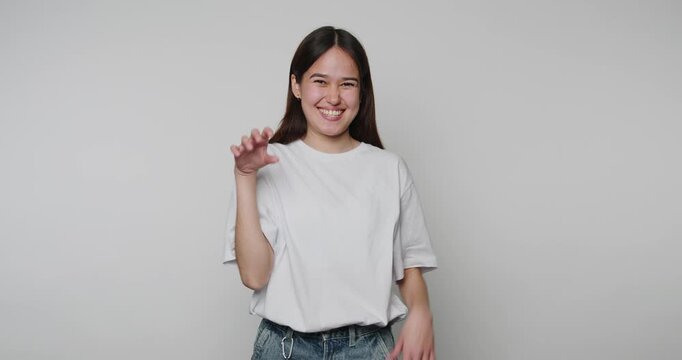 footage of young playful woman makes a claw gesture with her hands while smiling, radiating a fun and light-hearted atmosphere on beige background