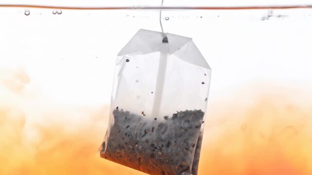 Close-up of a tea bag steeping in water, diffusing its warm orange color into the liquid, creating a peaceful and refreshing scene.